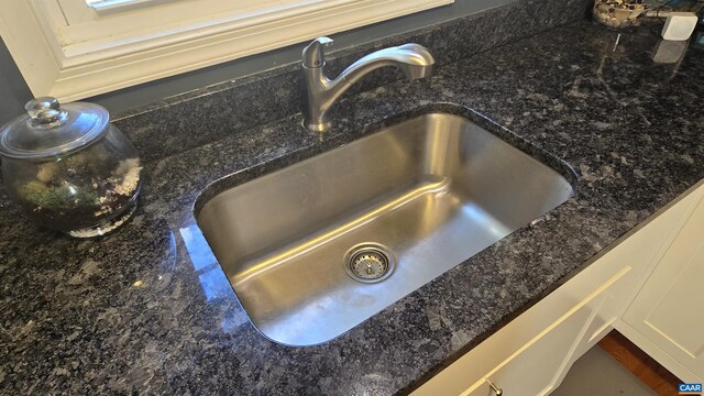 interior details with white cabinetry, dark stone counters, and sink