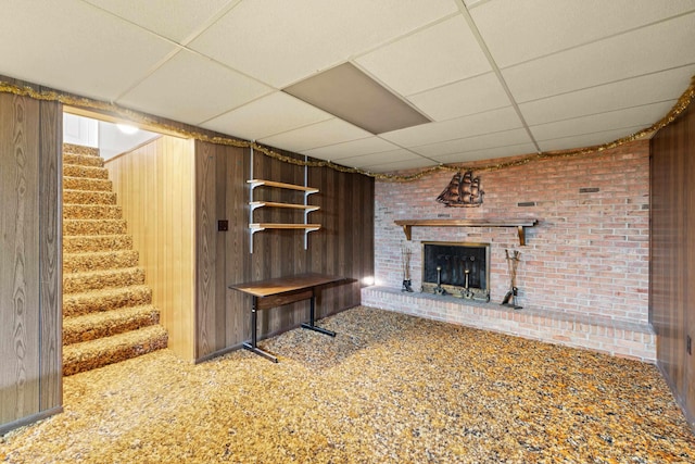 unfurnished living room featuring a paneled ceiling, carpet flooring, brick wall, a brick fireplace, and wood walls