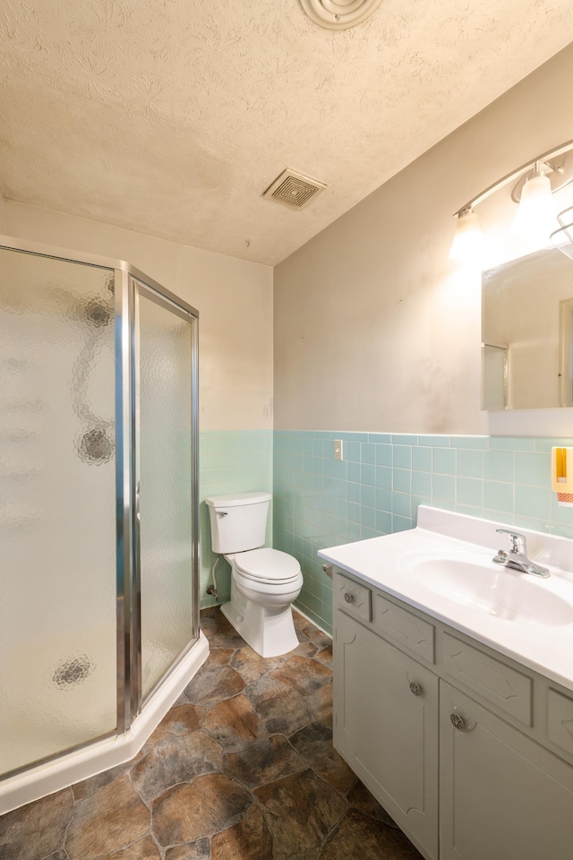 bathroom featuring vanity, a shower with door, tile walls, and a textured ceiling