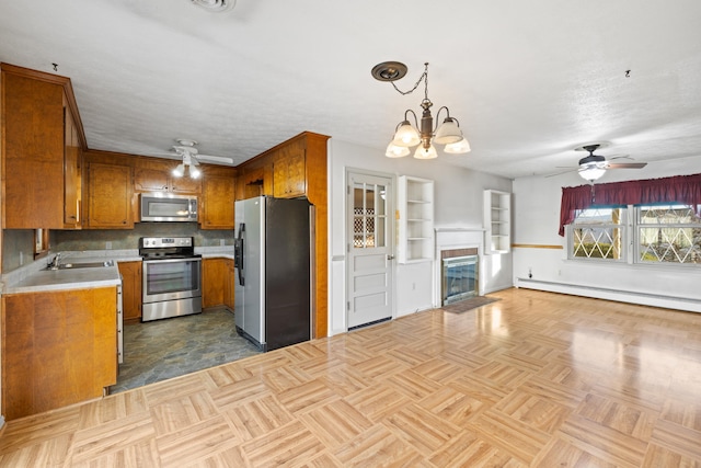 kitchen with sink, hanging light fixtures, stainless steel appliances, ceiling fan with notable chandelier, and a baseboard radiator