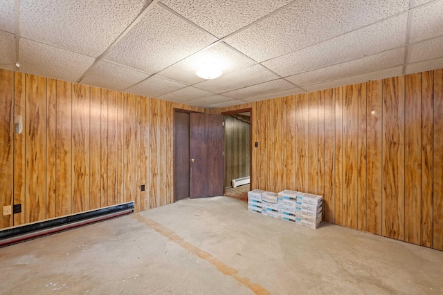 basement with a drop ceiling, baseboard heating, and wood walls