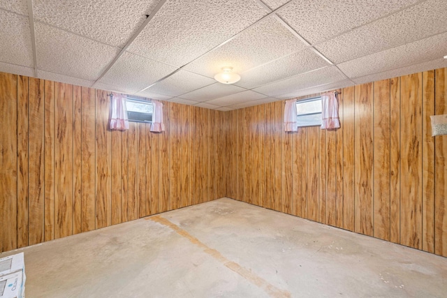 basement featuring a paneled ceiling and wood walls