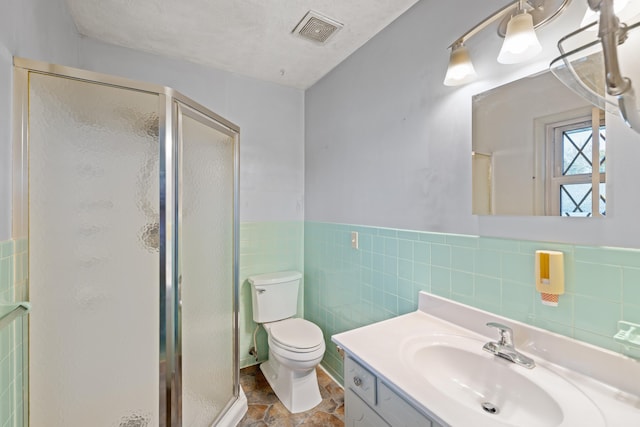 bathroom with vanity, toilet, tile walls, and a shower with shower door