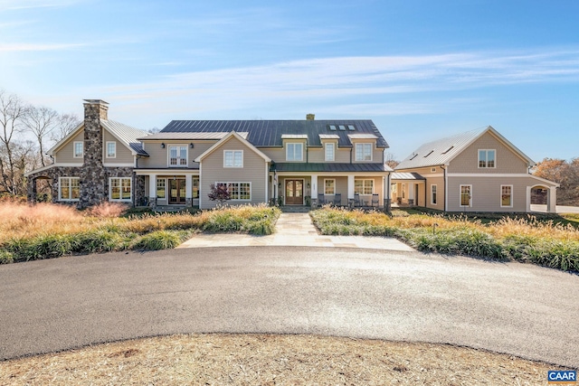 view of front facade featuring stone siding, a chimney, metal roof, covered porch, and a standing seam roof