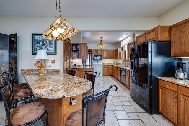 kitchen with a kitchen bar, a center island, hanging light fixtures, light stone countertops, and black appliances