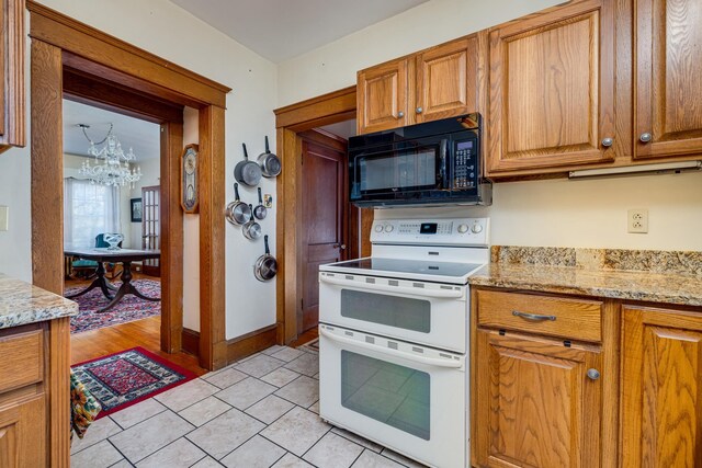 kitchen with range with two ovens, light stone countertops, light tile patterned floors, and a chandelier