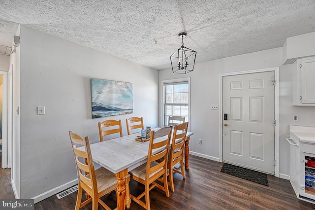 dining area featuring dark wood-style flooring, visible vents, a textured ceiling, a chandelier, and baseboards