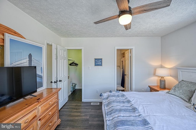 bedroom with ceiling fan, a walk in closet, a textured ceiling, and dark hardwood / wood-style flooring