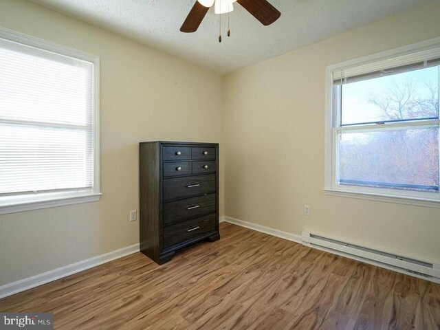 unfurnished bedroom featuring multiple windows, baseboard heating, and light hardwood / wood-style flooring