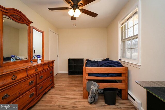 bedroom featuring ceiling fan, light hardwood / wood-style flooring, and a baseboard heating unit