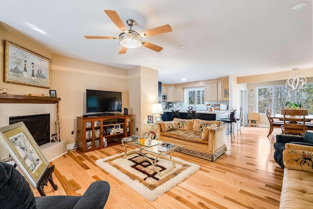 living room featuring ceiling fan with notable chandelier, a fireplace, and light hardwood / wood-style floors