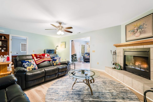 living room featuring a tile fireplace, ceiling fan, and light wood-type flooring