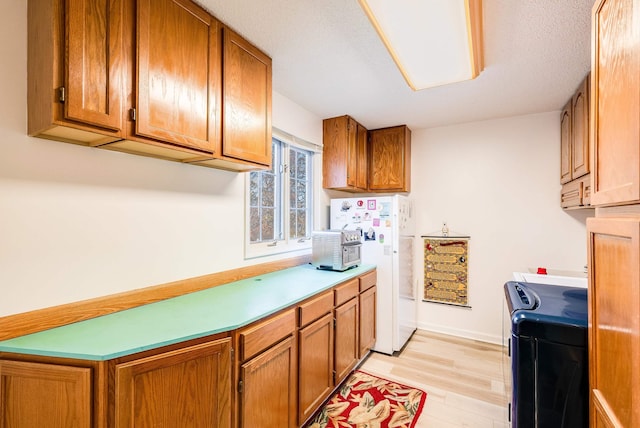 kitchen with a textured ceiling, white fridge, and light hardwood / wood-style flooring