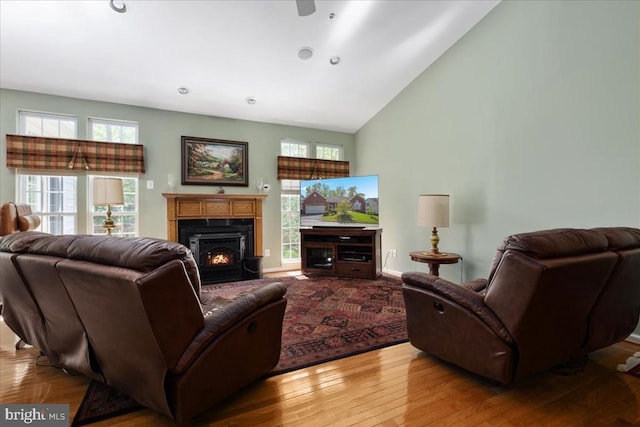 living room featuring a warm lit fireplace, high vaulted ceiling, plenty of natural light, and wood finished floors
