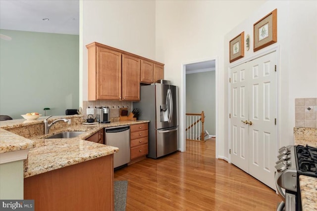 kitchen with appliances with stainless steel finishes, tasteful backsplash, a sink, a high ceiling, and light wood-style flooring