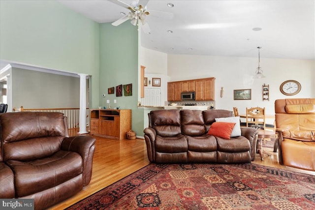 living area with decorative columns, high vaulted ceiling, ceiling fan, and wood finished floors
