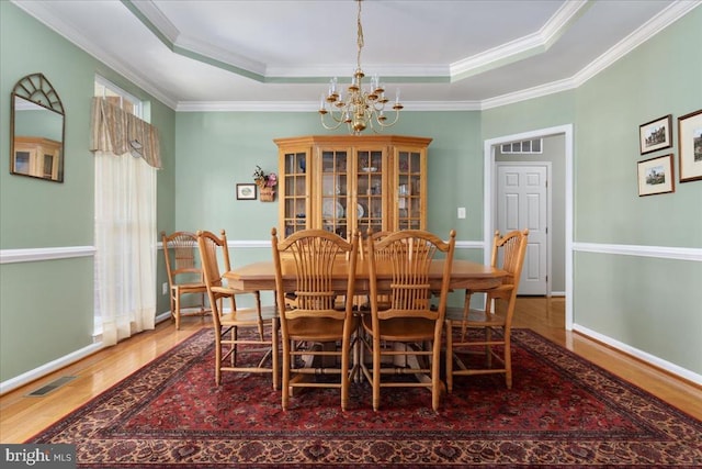 dining room featuring crown molding, a raised ceiling, wood finished floors, and a chandelier