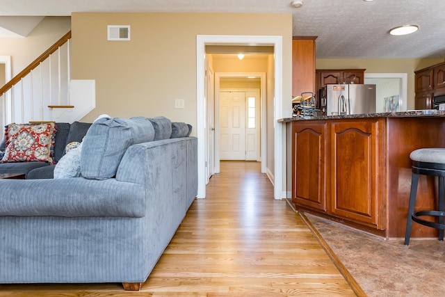 living area with light wood-type flooring, stairs, visible vents, and a textured ceiling