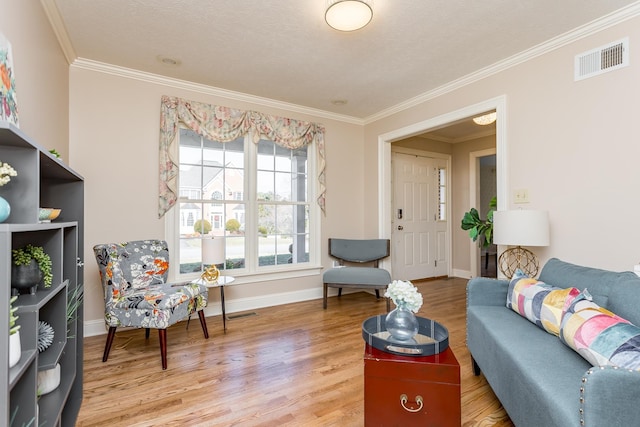 living room with ornamental molding, light wood-type flooring, visible vents, and baseboards