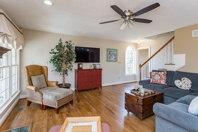 living room with ceiling fan, wood finished floors, visible vents, baseboards, and stairs