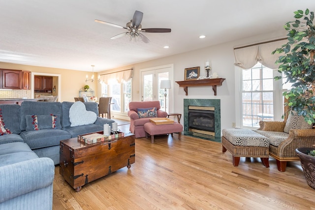 living room with ceiling fan with notable chandelier, a high end fireplace, light wood-style flooring, and recessed lighting