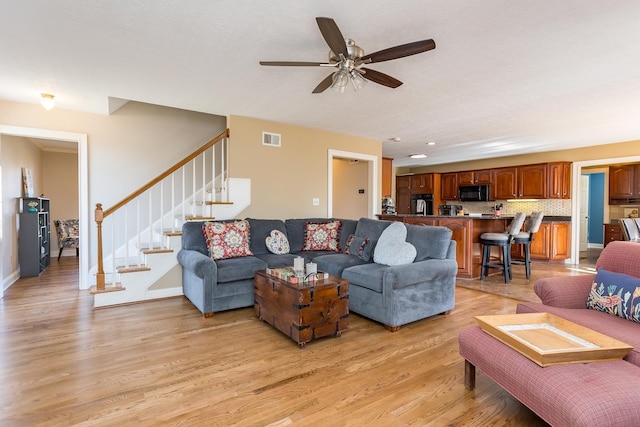 living area featuring visible vents, stairway, light wood-style floors, ceiling fan, and baseboards