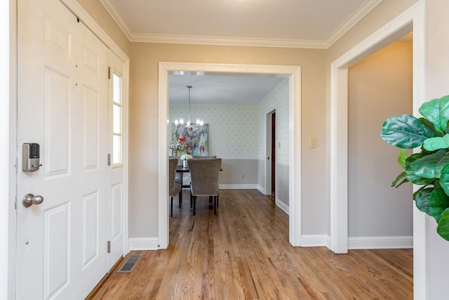 entryway featuring a chandelier, visible vents, baseboards, light wood-style floors, and crown molding