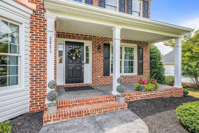 entrance to property featuring a porch and brick siding