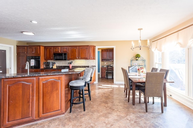 kitchen with pendant lighting, a notable chandelier, backsplash, dark stone countertops, and black microwave