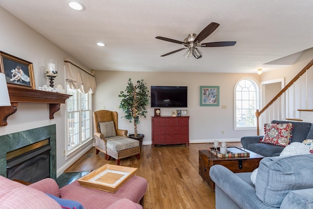 living room with a glass covered fireplace, plenty of natural light, stairway, and wood finished floors