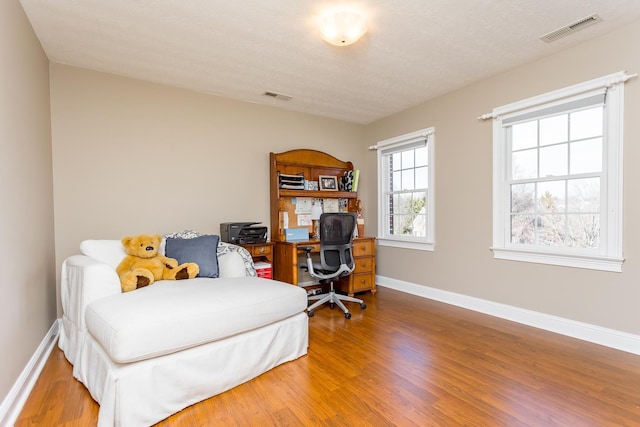 bedroom with a textured ceiling, wood finished floors, visible vents, and baseboards