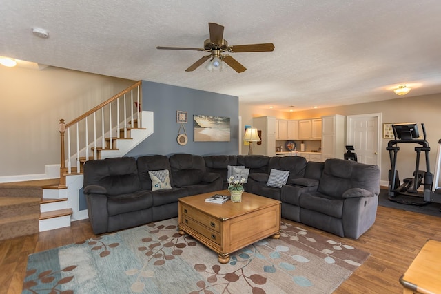 living area featuring stairs, a textured ceiling, wood finished floors, and baseboards