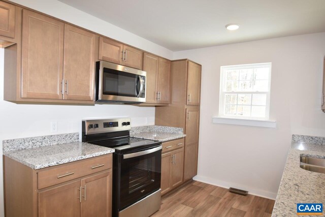 kitchen with light stone counters, sink, light hardwood / wood-style floors, and appliances with stainless steel finishes