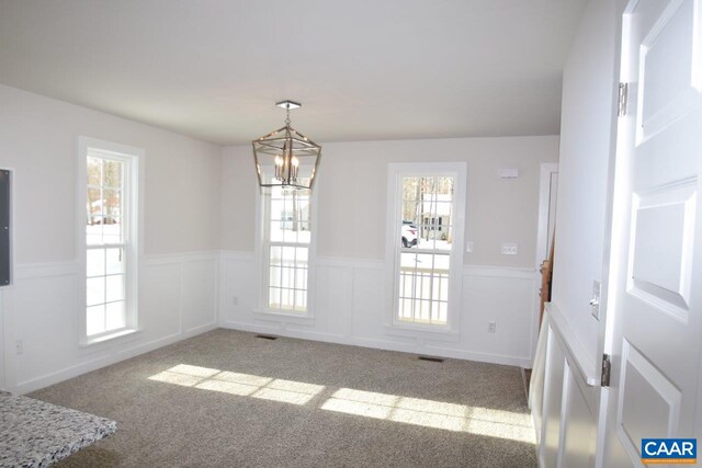 unfurnished dining area featuring light carpet, plenty of natural light, and a chandelier