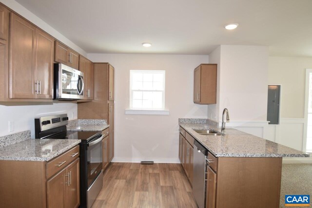 kitchen featuring stainless steel appliances, kitchen peninsula, sink, and light stone countertops