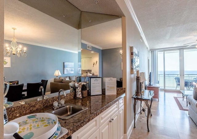 kitchen featuring white cabinets, ornamental molding, sink, dark stone counters, and a textured ceiling