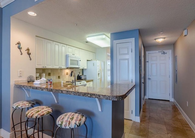 kitchen with kitchen peninsula, white appliances, tasteful backsplash, white cabinets, and light tile floors