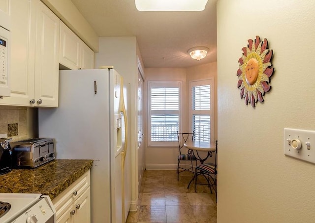 kitchen featuring white cabinets, light tile flooring, backsplash, dark stone counters, and stove