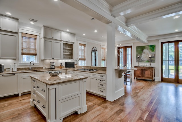 kitchen featuring beamed ceiling, light wood-type flooring, ornamental molding, sink, and a kitchen island