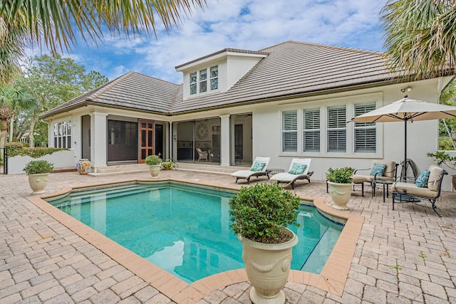 back of house with stucco siding, a tile roof, a sunroom, an outdoor pool, and a patio area