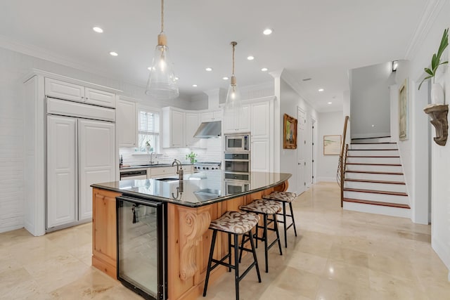 kitchen with a sink, wine cooler, under cabinet range hood, dark countertops, and a kitchen breakfast bar