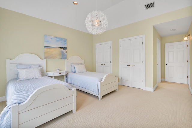 bedroom with visible vents, light colored carpet, baseboards, and multiple closets