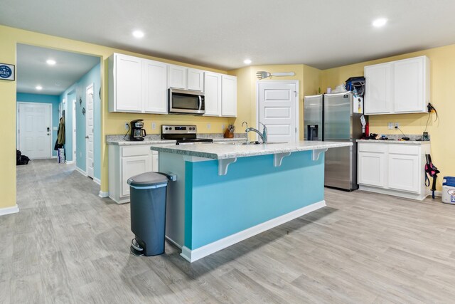 kitchen with a kitchen island with sink, light hardwood / wood-style flooring, stainless steel appliances, and white cabinets