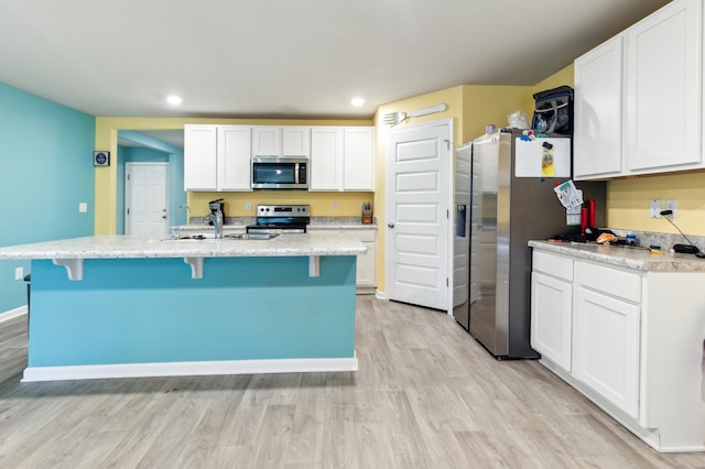 kitchen with a kitchen island with sink, appliances with stainless steel finishes, white cabinets, and light hardwood / wood-style floors