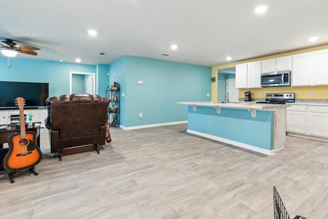 kitchen with a center island with sink, appliances with stainless steel finishes, white cabinets, and light hardwood / wood-style floors