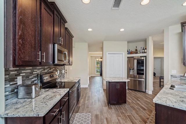 kitchen with light stone counters, stainless steel appliances, dark wood-type flooring, and a kitchen island