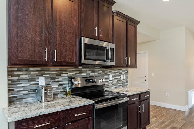 kitchen featuring decorative backsplash, dark brown cabinets, stainless steel appliances, light stone countertops, and hardwood / wood-style flooring