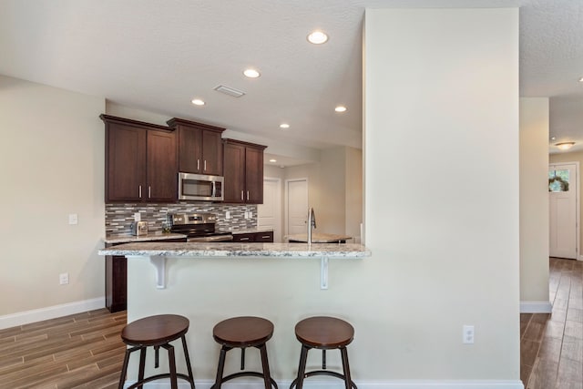 kitchen featuring light stone countertops, a breakfast bar area, appliances with stainless steel finishes, and dark hardwood / wood-style flooring