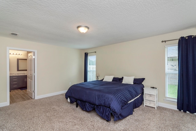 carpeted bedroom featuring ensuite bathroom, multiple windows, and a textured ceiling