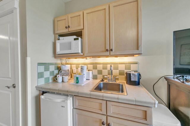 kitchen featuring tile counters, refrigerator, light brown cabinets, backsplash, and sink